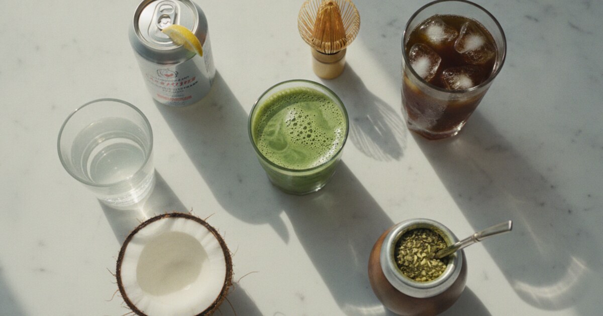 Flat-lay of matcha, cold brew coffee, yerba mate, sparkling water, and coconut water arranged as healthy energy drink alternatives on a white marble surface